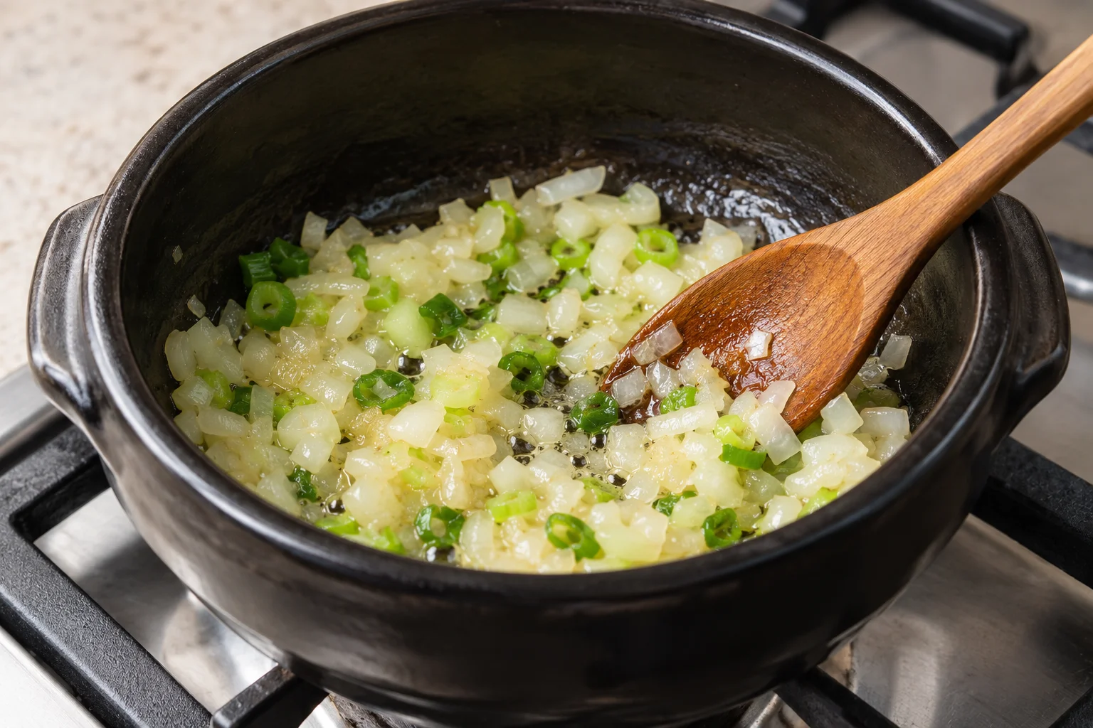 Onion and green onion sauteing in oil in a black pot